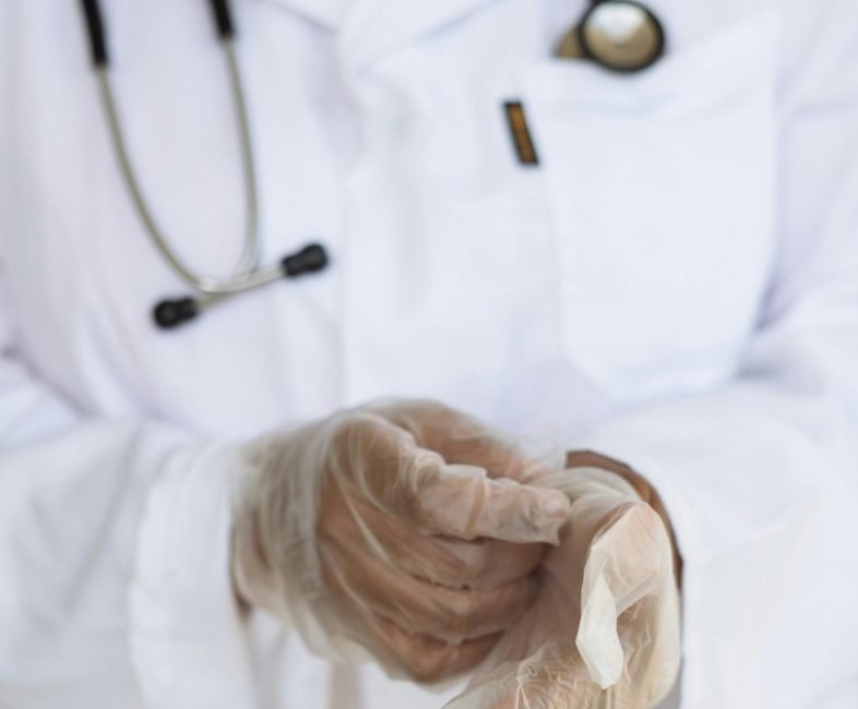 pexels-photo-3825586-3825586 Faceless ethnic medical worker in lab coat and stethoscope taking of transparent gloves after approaching patients for examination in modern hospital